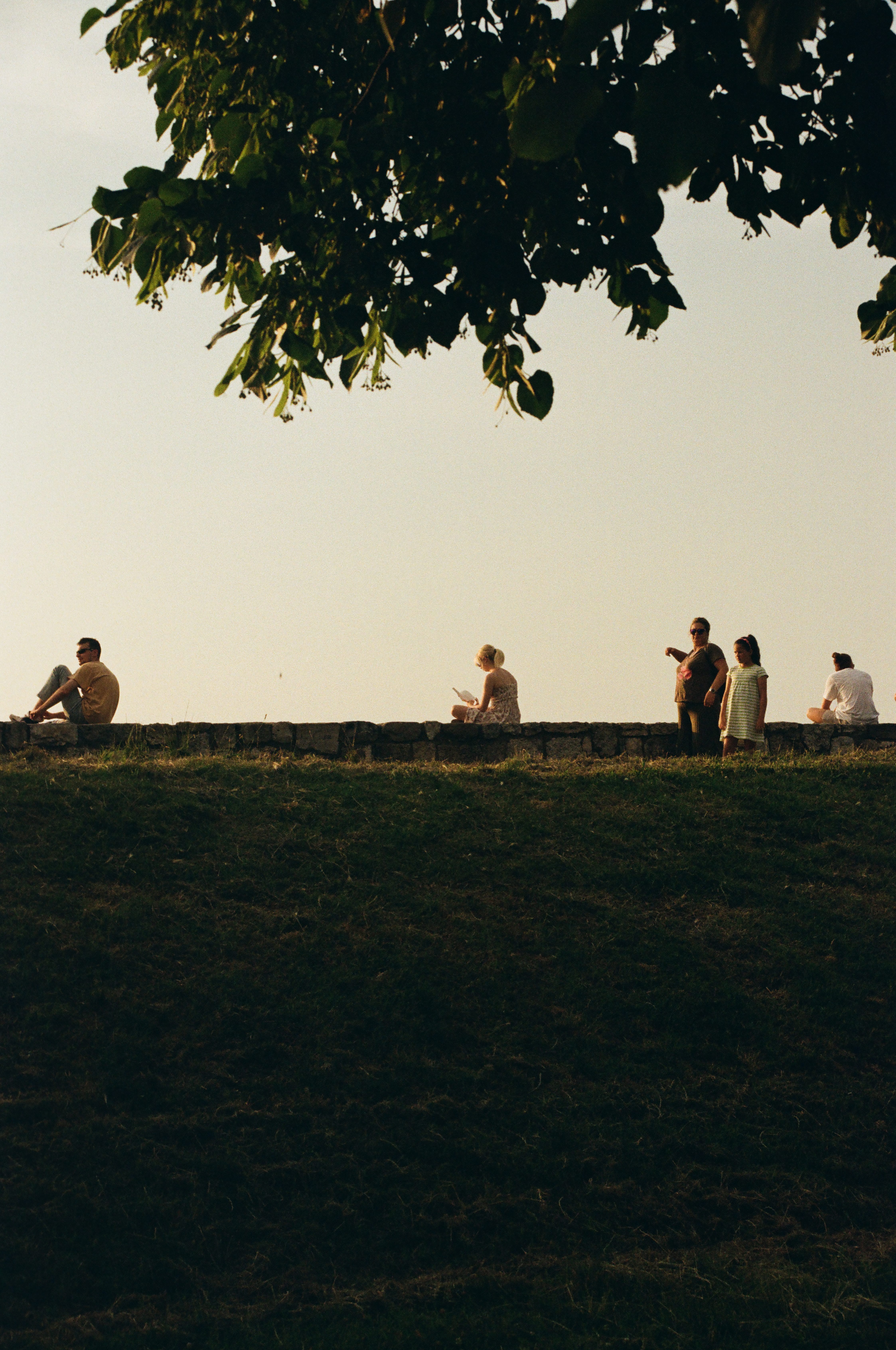 Girl sits on the edge of a wall at Kalemegdan Fortress reading a book at sunset