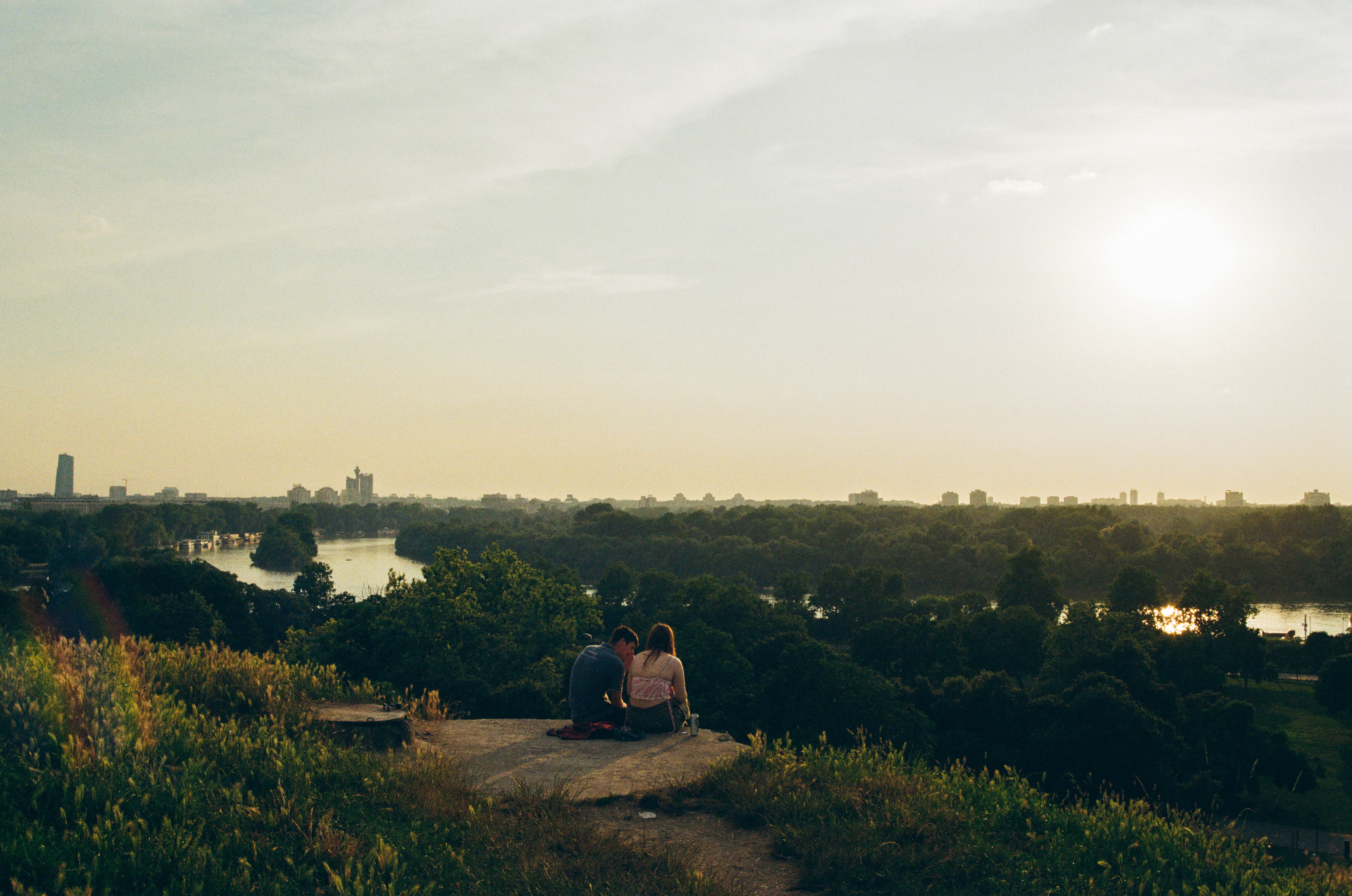 Couple sits on a rock at Kalemegdan Park overlooking the St Sava River in Belgrade during sunset
