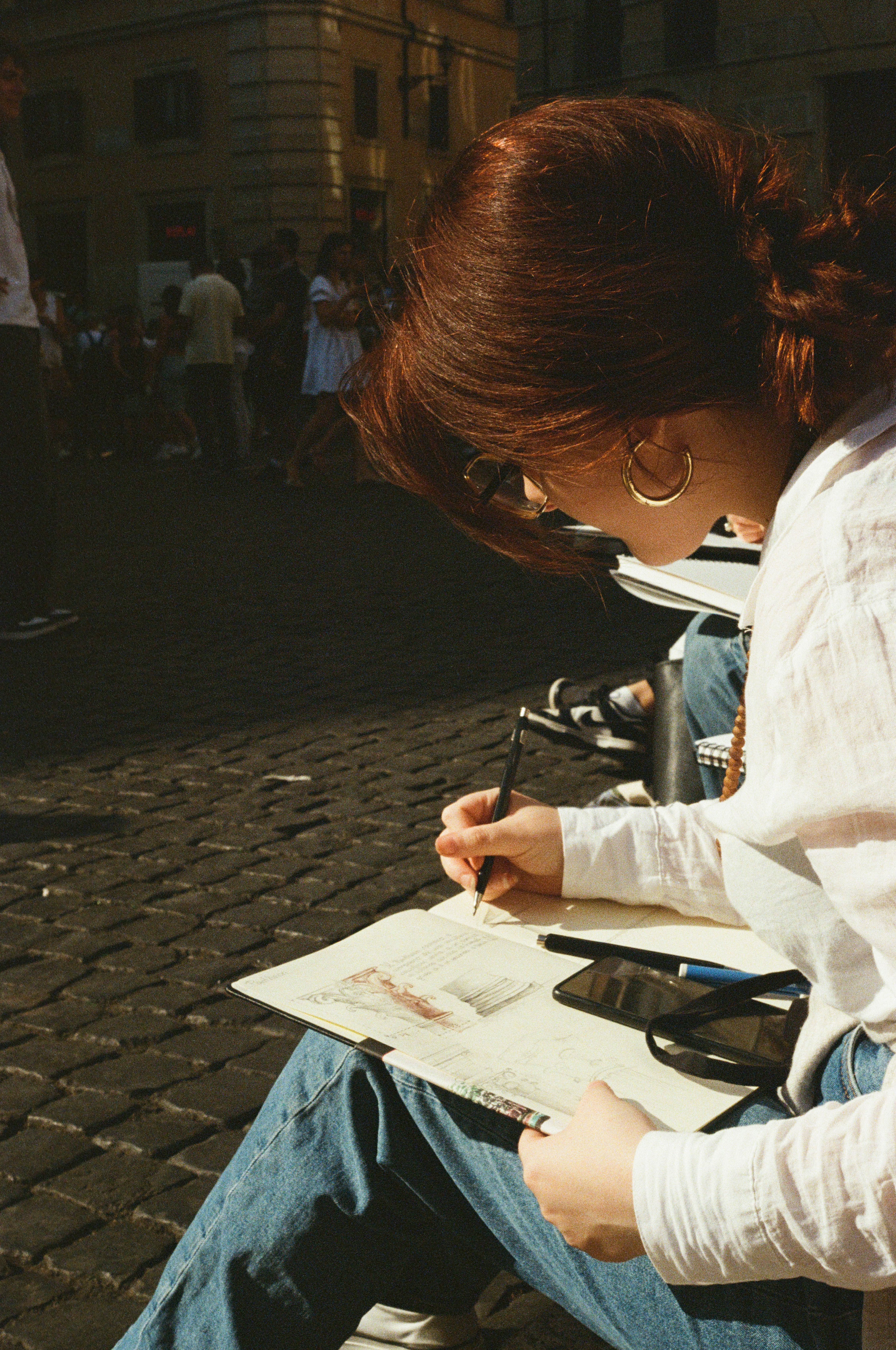 Girl leans over her sketchbook to draw while sitting on stair steps in Rome