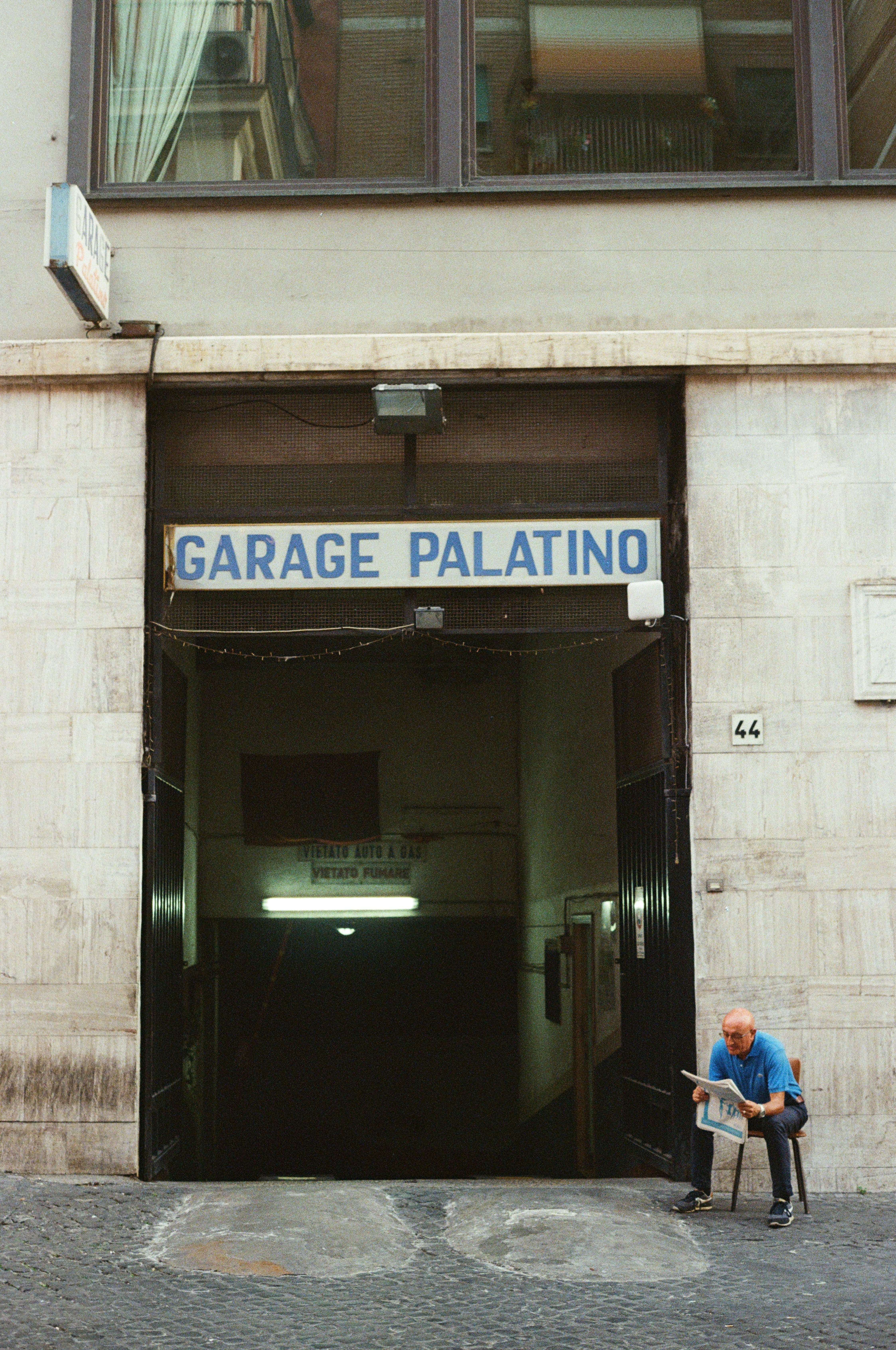 Man sits on a chair reading a newspaper in front of a garage entrance in Rome, Italy
